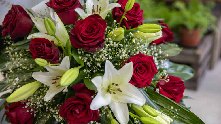 Kukkakaupan hautaijaiskukkalaitteessa punaisia ja valkoisia kukkia.