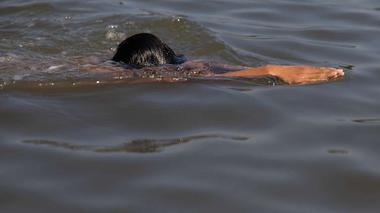 Photo shows a child swimming in a lake.