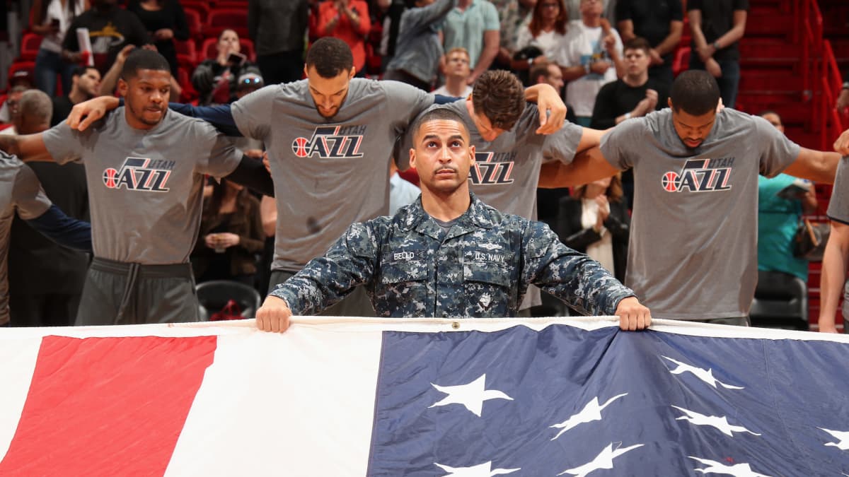Yhdysvaltain merijalkaväen sotilas pitelee Yhdysvaltain lippua NBA-koripalloilijoiden edessä.