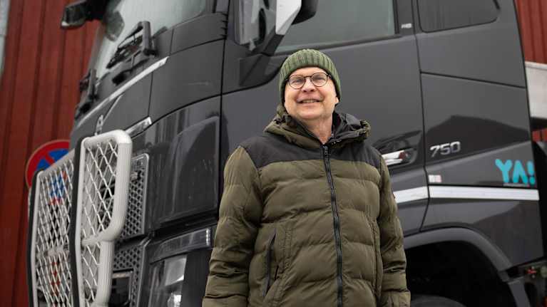 En man (Henrik Östman) med glasögon, grön vinterjacka och grön mössa framför en stor lastbil.
