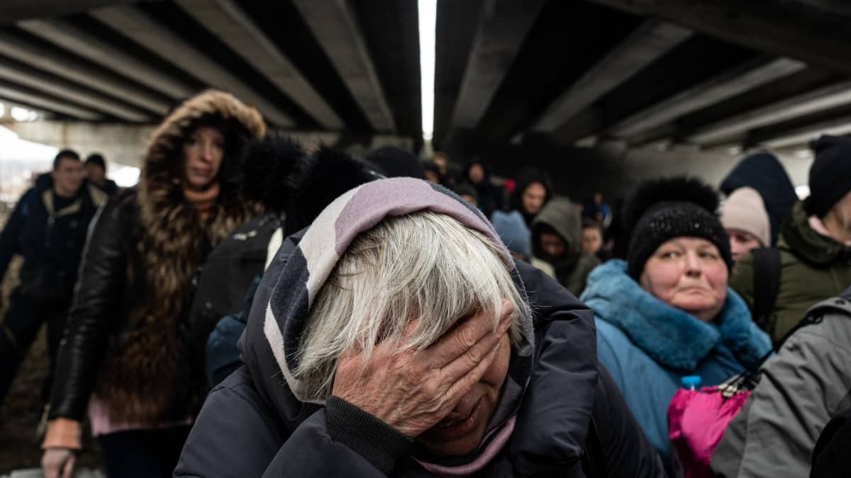 Naine etuetuallal peittää kädellään silmänsä, taustalla muita pakenevia ukrainalaisia.