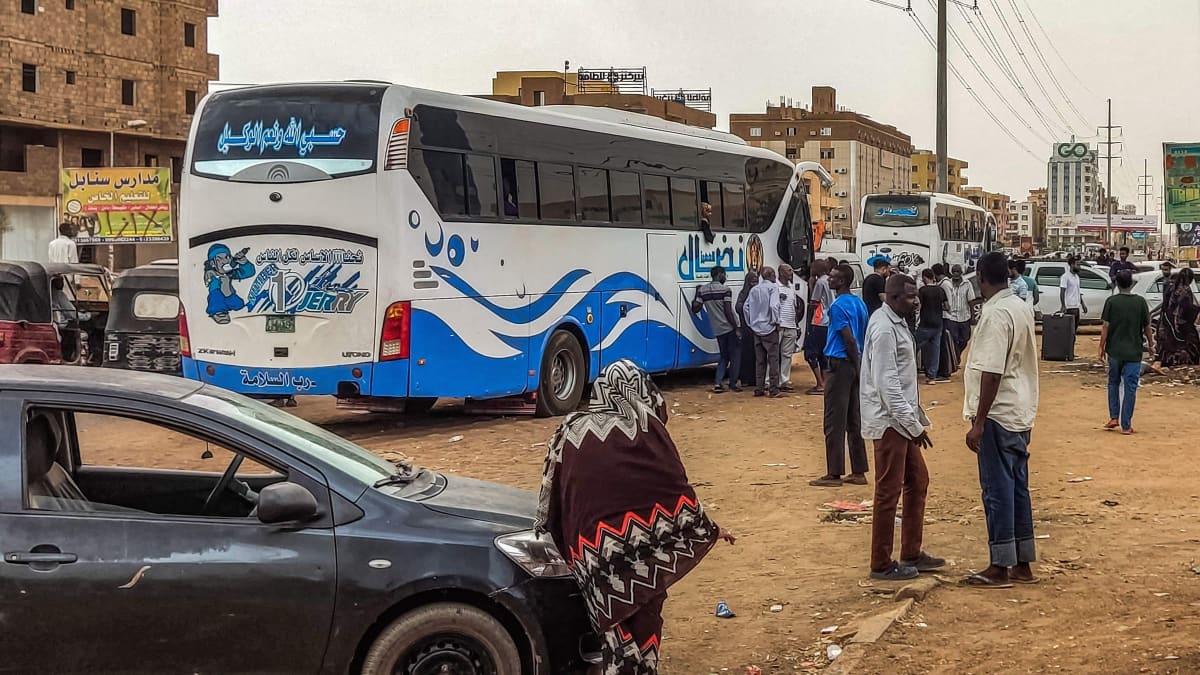 Ihmiset odottavat matkatavaroiden kanssa Khartumista lähtevää bussia.