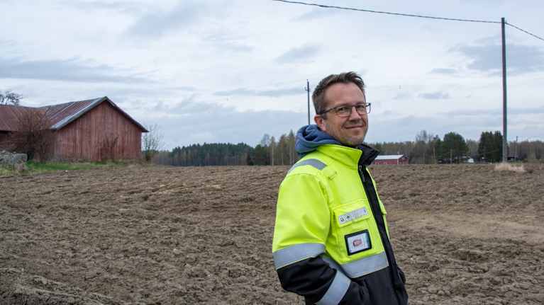 Man i gul jacka står på åker och tittar in i kameran.