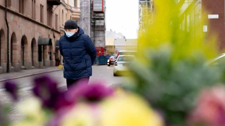 Vanha mies kävelee tien yli kasvosuojain päässä.