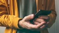 Closeup of a person wearing a gold coloured hoodie holding a smartphone with both hands.