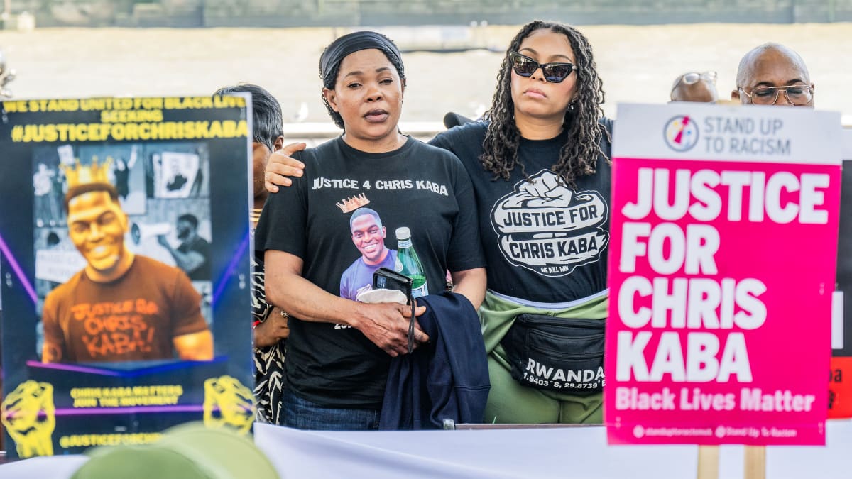 Kaksi naista ja kylttejä, joissa vaaditaan oikeutta Chris Kaballe. Yhdessä kyltissä ja toisen naisen paidassa on Kaban valokuva.