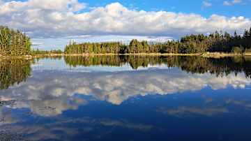 Rauhallinen merimaisema heijastuu tyynestä veden pinnasta, taustalla sininen taivas ja pilviä.