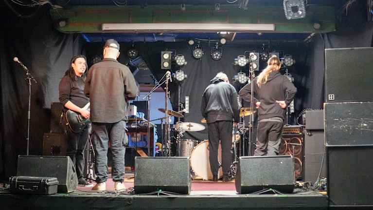 En grupp personer står på en scengolv framför musikutrustning och instrument.