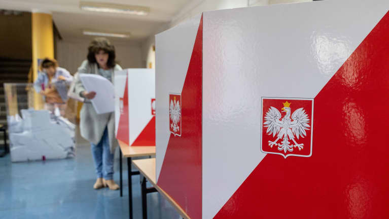 Nainen äänestyspaikalla. Etualalla äänestyskoppi, jonka seinässä on Puolan vaakuna.