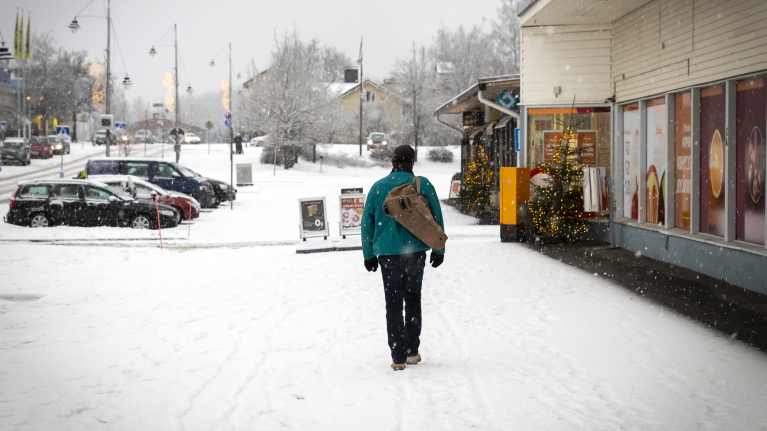 Mies kävelee Kuhmoisten keskustassa lumisateessa.