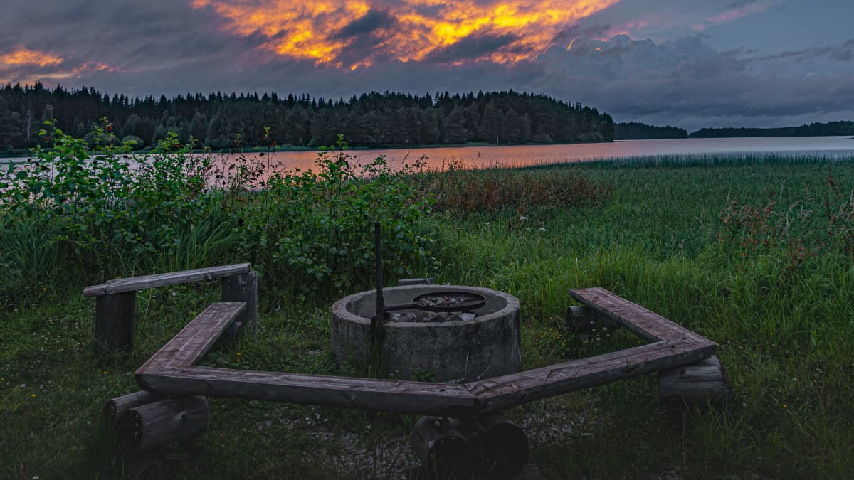 Auringonlasku Keuruulla. Järven rannalla nuotiopaikka, iltaruskoa ja pilviä. 
