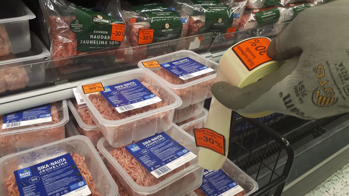 Jauhelihapakkauksia joissa punaisia alennustarroja. Kaupan työntekijän kädessä on rullalla lisää alennustarroja.