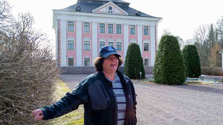 Bilden föreställer en kvinna som står framför en stor, rosa slottssbyggnad med flera våningar.