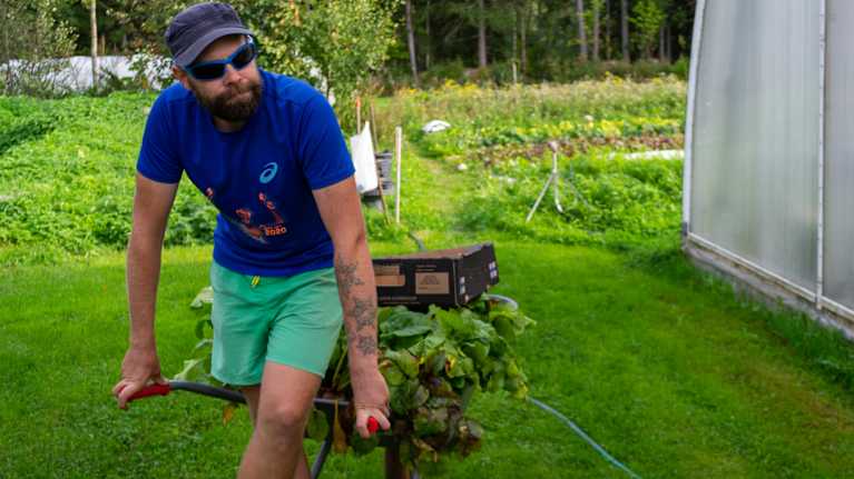 En man med keps och solglasögon lutar sig mot en skottkärra.