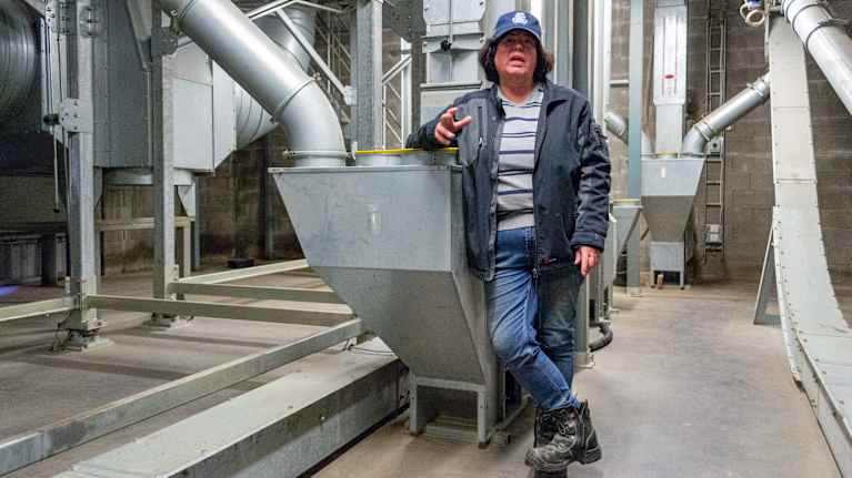 En kvinna står lutad mot en maskin i en industriell anläggning och är klädd i arbetskläder.