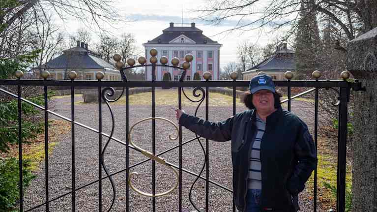 En person står lutad mot en vacker smidesgrind framför ett stort slott med rosa detaljer. 