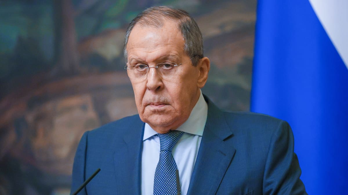 Sergej Lavrov klädd i kostym står framför en mikrofon. Han ser allvarlig ut. I bakgrunden Rysslands flagga.