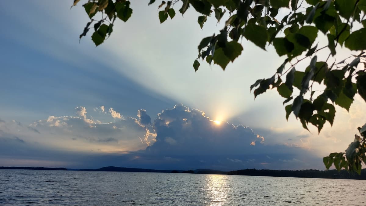 Kumpupilviä järven takana, auringonsäteet kurkistavat pilven takaa. 