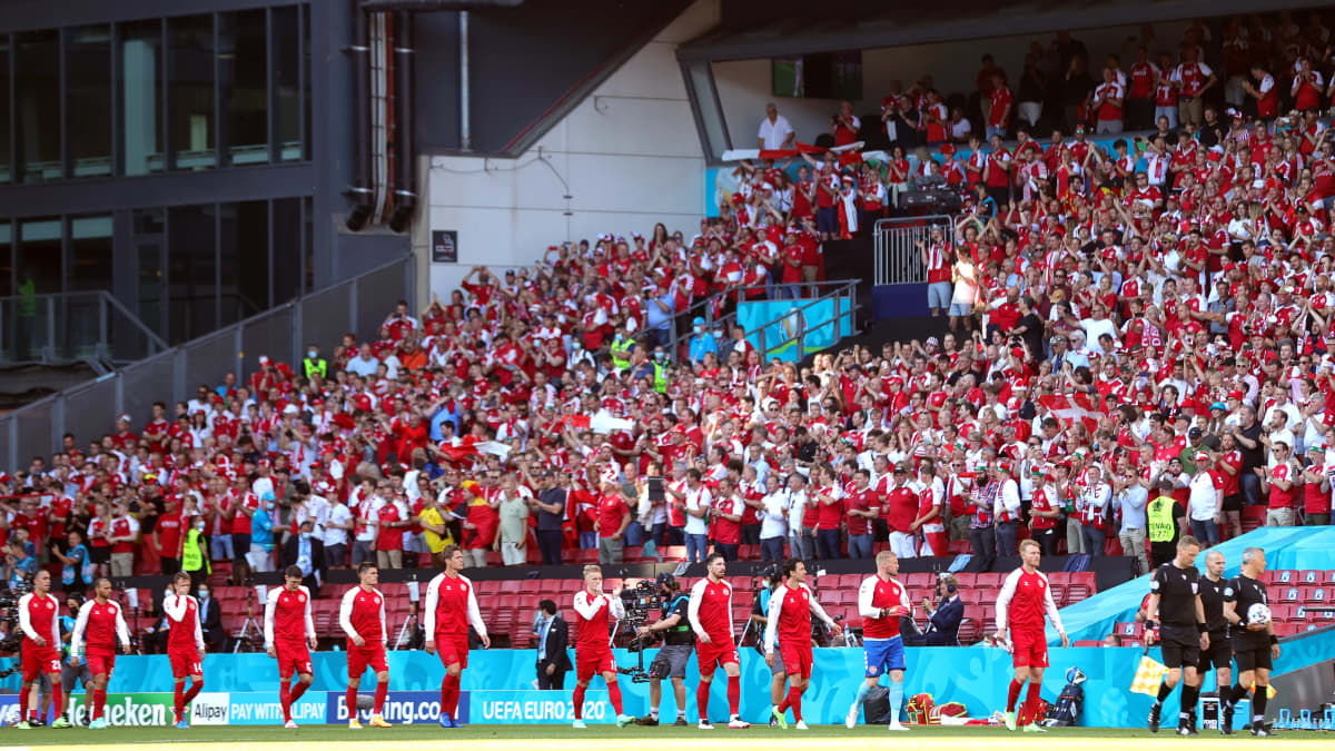 Tanskan joukkueen pelaajat kävelevät stadionilla. Katsomo on täynnä väkeä.