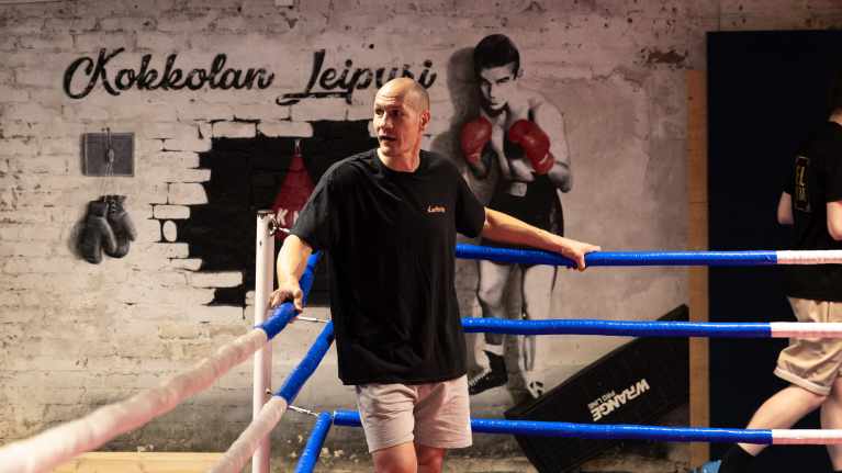 Nyrkkeilyvalmentaja Amin Asikainen nojaa kehän sinisessä päädyssä köysiin.