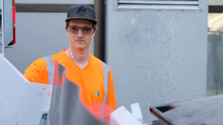 L & T:n jäteautonkuljettaja Tuure Vanhanen tyhjentämässä roskalaatikkoa jäteautoon.