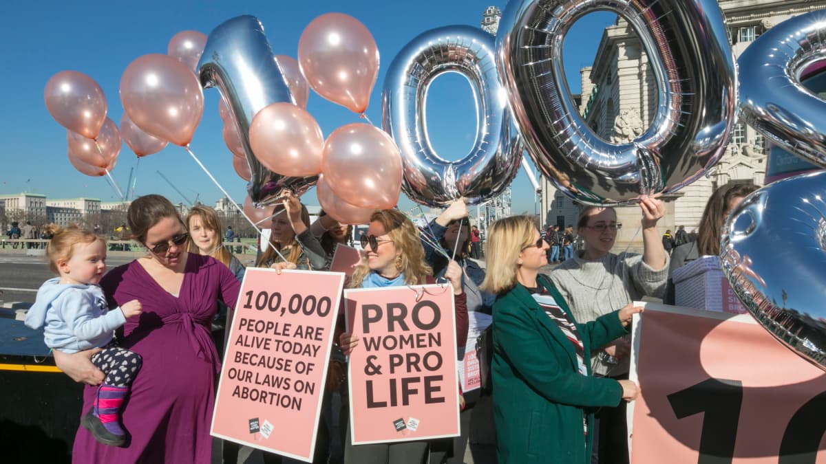 Aborttia vastustavat naiset kantavat kylttejä ja ilmapalloja Pohjois-Irlannin toimiston edustalla helmikuussa 2019. Kyltissä lukee: sata tuhatta ihmistä on elossa aborttilakiemme ansiosta.