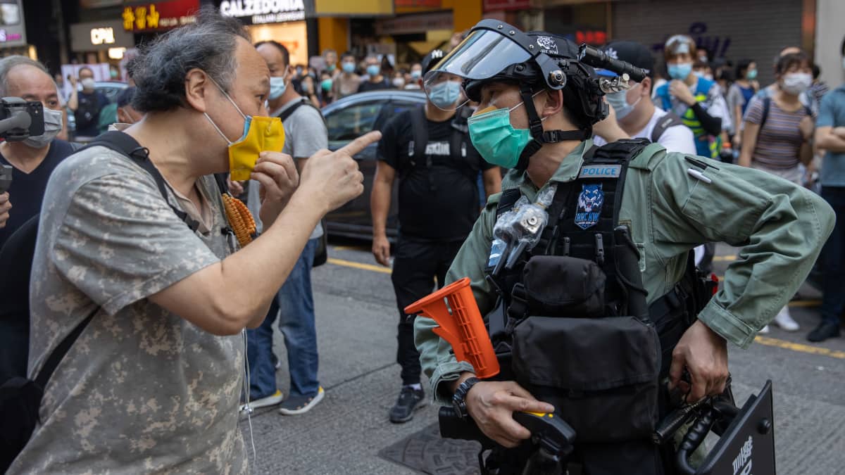 Mielenosoittaja osoittaa sormella poliisia, molemmilla kasvomaskit.