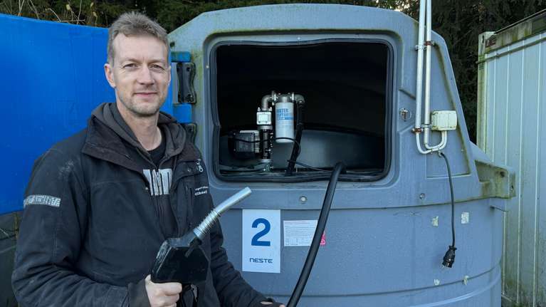 En man står vid en blå dieseltank märkthåller i ett bränslepumppistol.