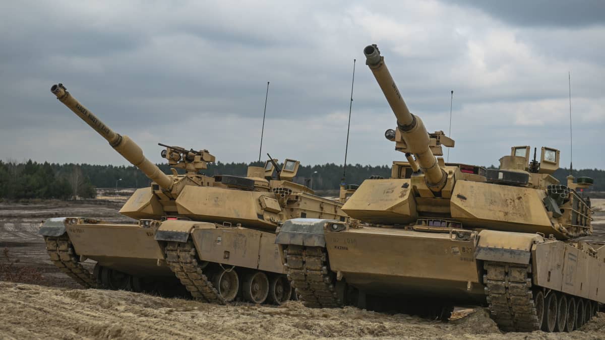 Abrams-taisteluajoneuvoja seisoo vierekkäin hiekkaisella maalla.