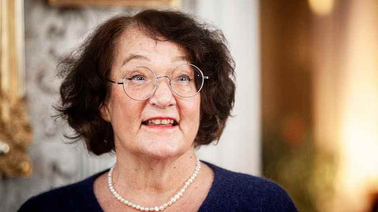 En kvinna, Monika Fagerholm, i bl� tr�ja och p�rlhalsband tittar leende f�rbi kameran.