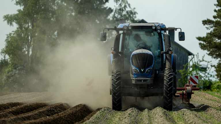 Traktor i arbte på dammig åker.