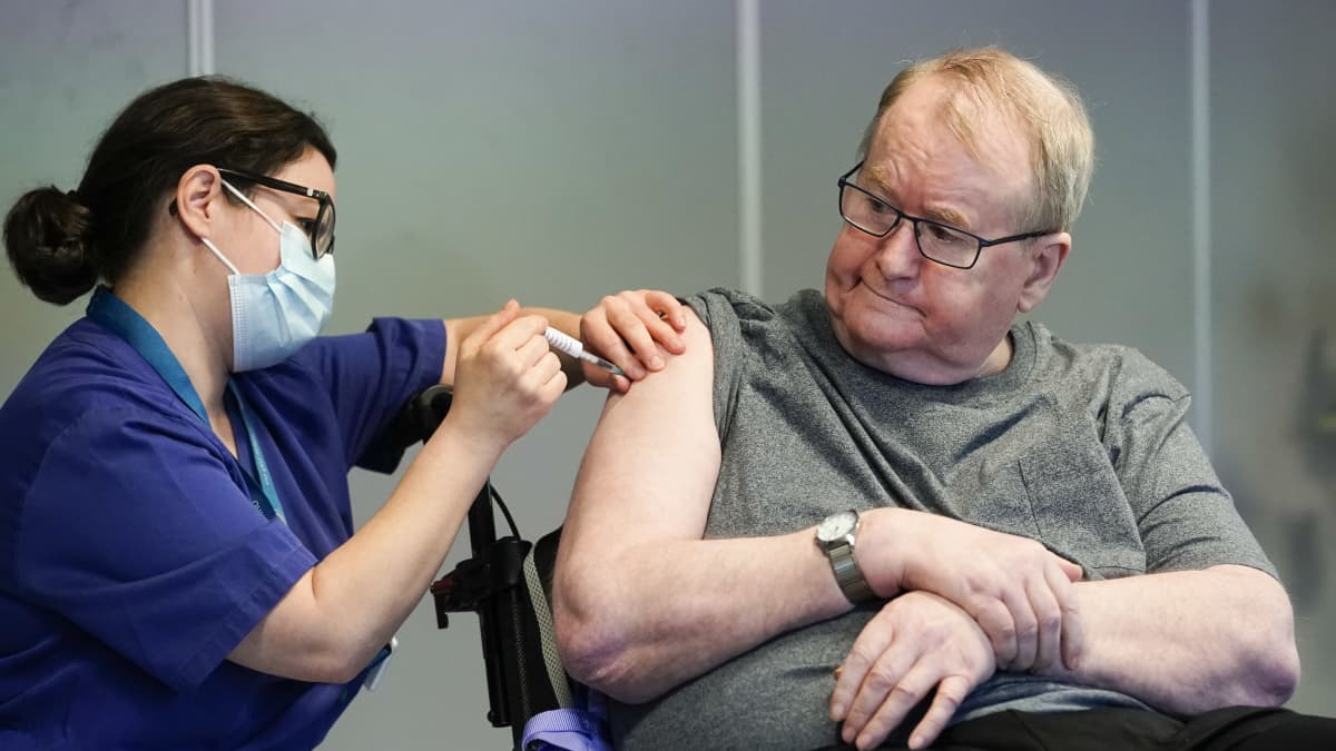 Man på servicehem får vaccin i armen av vårdpersonal med munskydd.