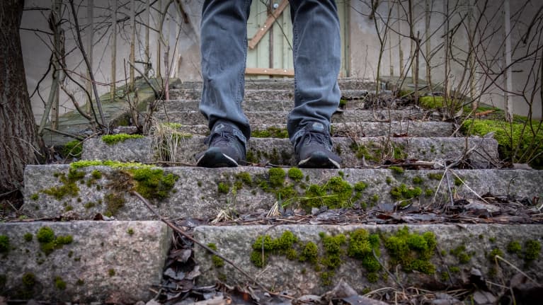 Lähikuvassa mies seisomassa sammaloituneilla portailla.