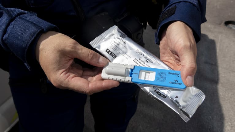 Huumausainepikatesti käsissä pideltynä kääreiden päällä. Negatiivinen testitulos, kolme punaista viivaa.