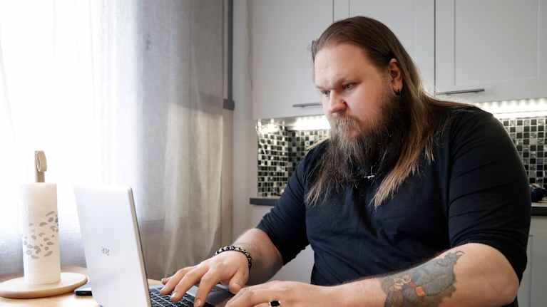 Mies kirjoittaa kannettavalla tietokoneella keittiön pöydän ääressä. 