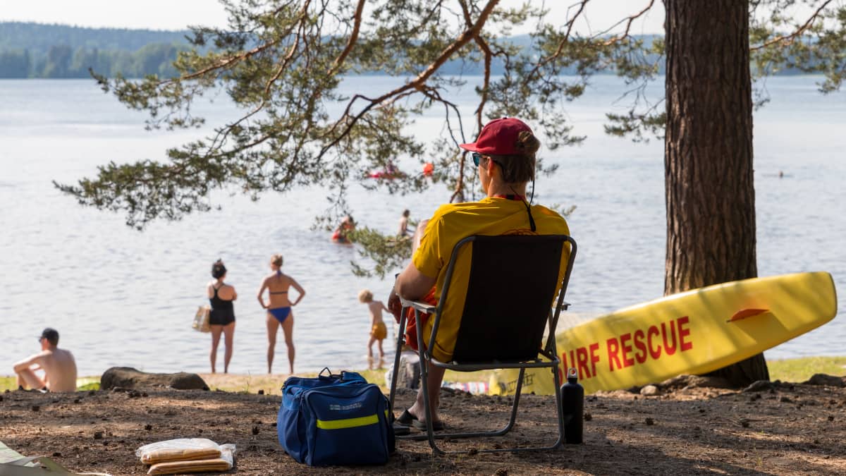 A lifeguard sits in a chair with people standing and sitting on the beach in the background at Tuomiojärvi beach in Jyväskylä. 
