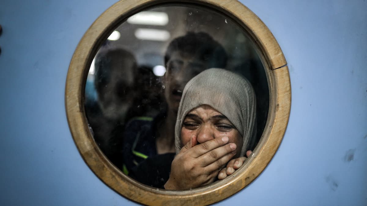 Palestiinalainen nainen katsoo sairaalan oven ikkunan läpi itkien haavoittuneita.