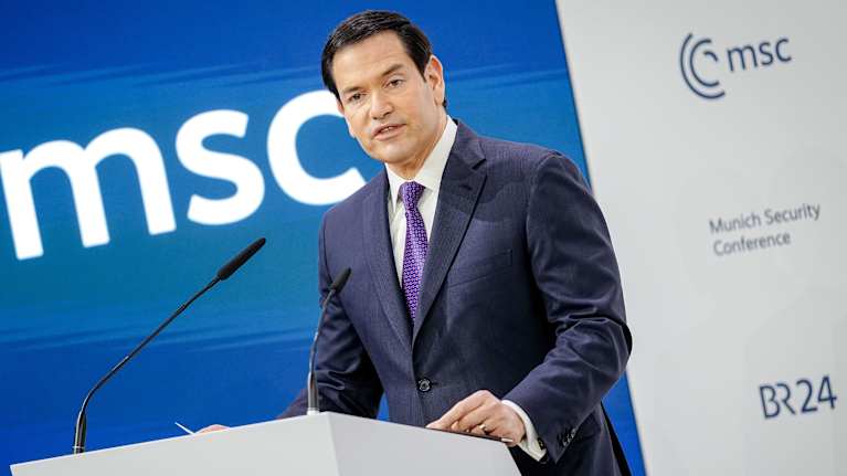 Marco Rubio i en mörkgrå kostym och lila slips står vid ett talarpodium och pratar. I bakgrunden syns logon "MSC" på en vägg.