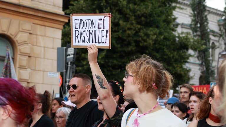 People of different ages march in Helsinki, with one woman holding a sign that reads "Absolutely against racial discrimination!" (Finnish) 