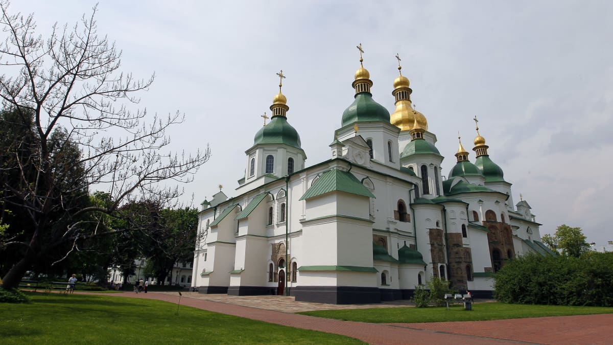 Vaaleaseinäinen kirkko, jossa vihreät tornit ja kullatut kupolit. 