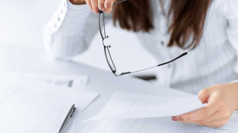 Woman holding eyeglasses and looking at paperwork.