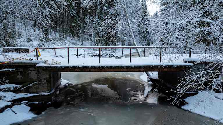 Winter landscape with a partially frozen river flowing under an old bridge covered in snow.