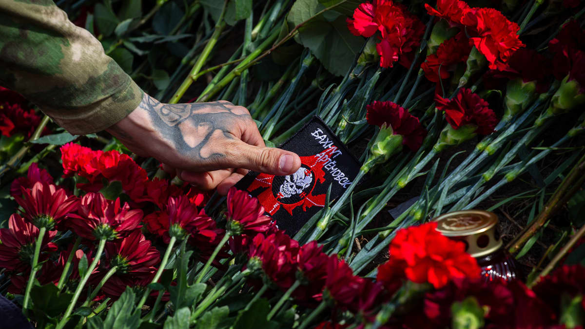 Tatuoitu käsi painaa Wagnerin logolla varustetun kangasmerkin punaisten kukkien keskelle.