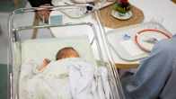 A newborn is lying under a blanket inside a crib in a hospital setting. 