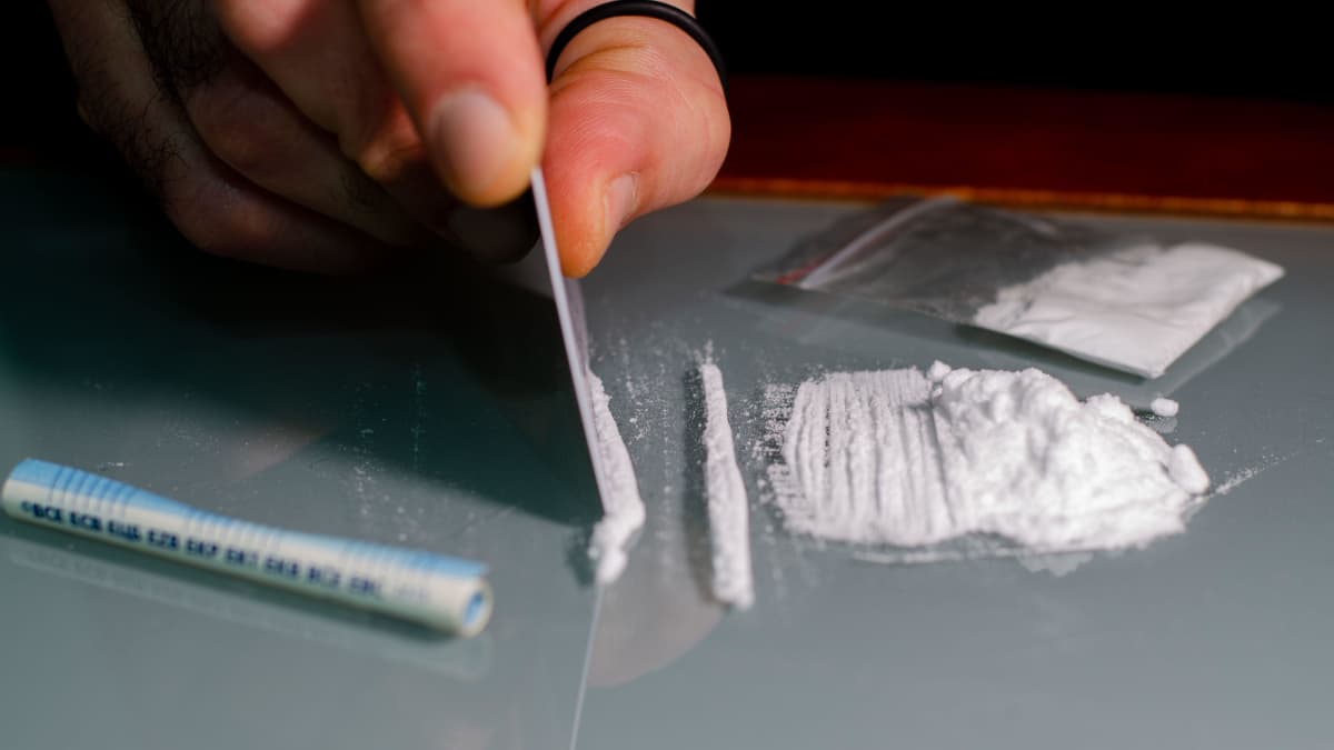 A person using a credit card to divide lines of cocaine on a table.