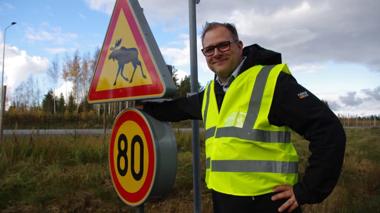 En man i reflexväst står vid en trafikskylt.