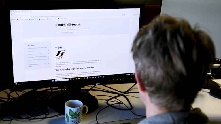 The photo shows a person sitting in front of a computer.