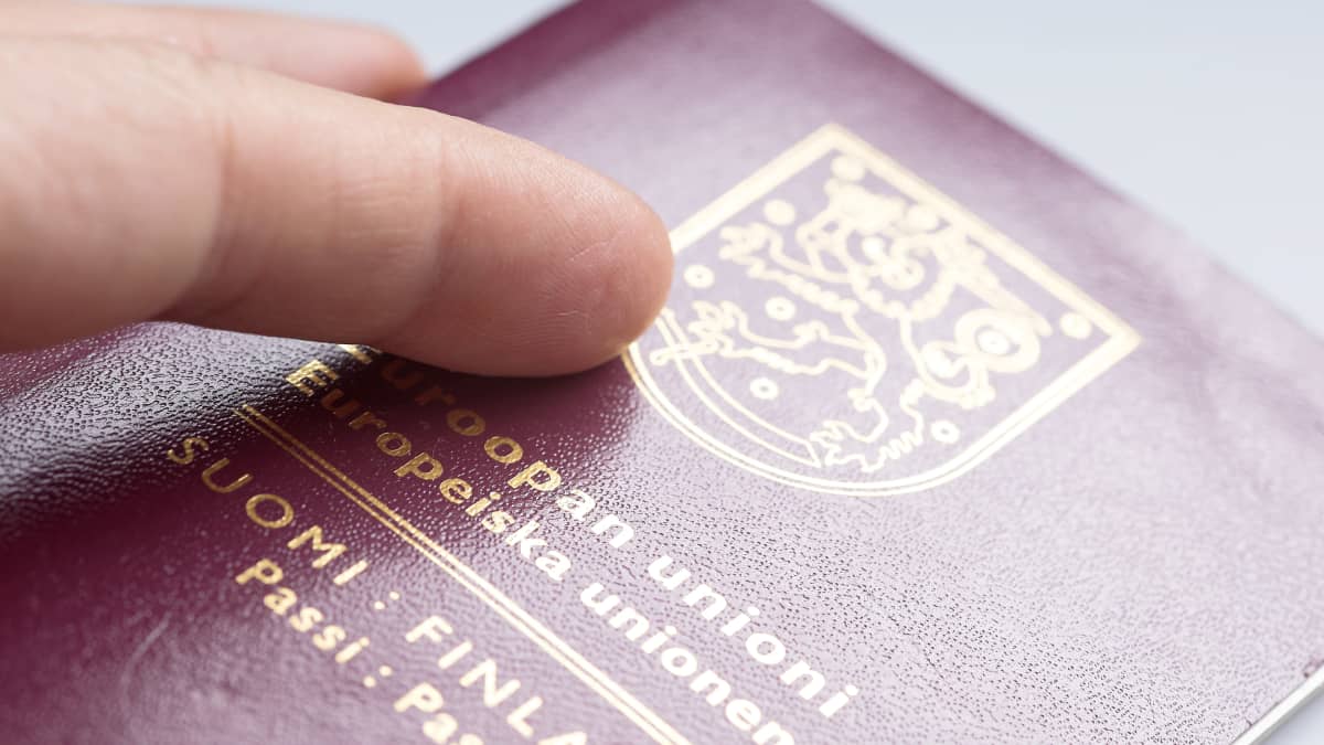 Close-up photo of a burgundy Finnish passport with a finger on top of it.