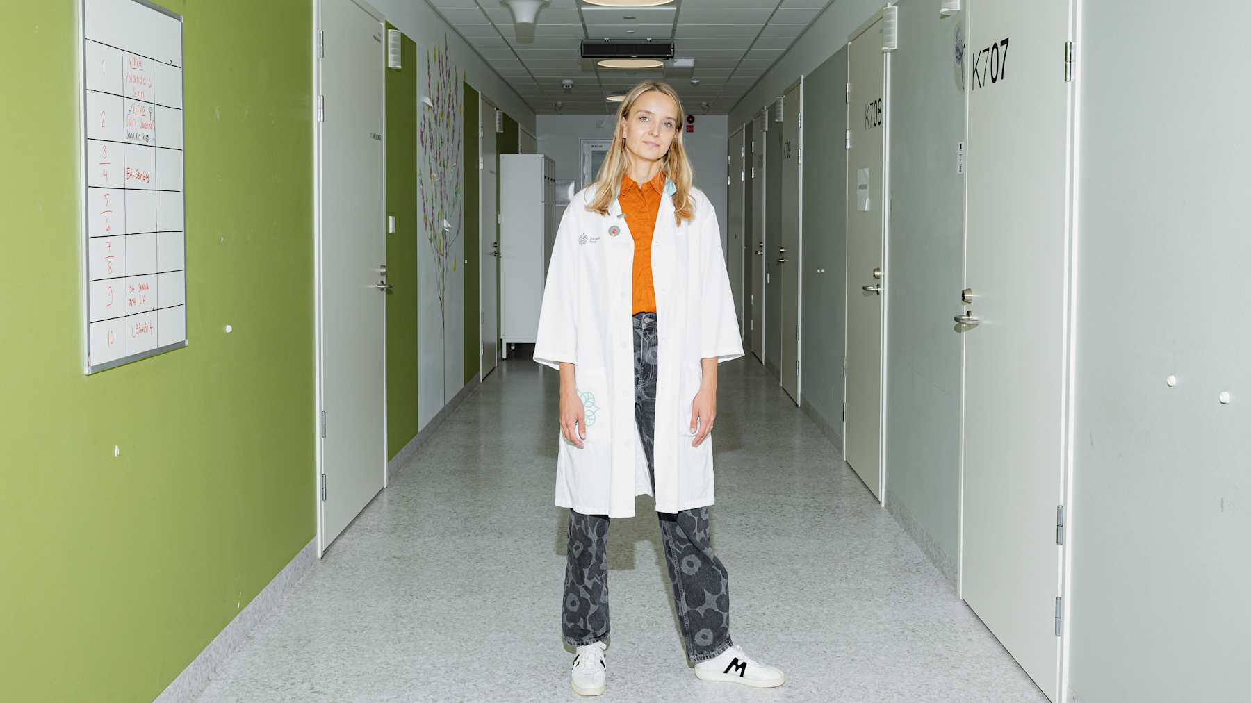 Lääkärinasuinen nainen seisoo sairaalan käytävällä.