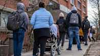 People in standing in line outside a red brick building in early spring.